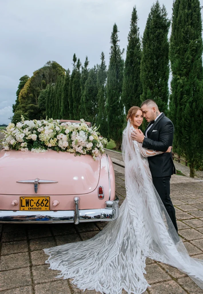 Recuerdo eterno de pareja casada frente a un auto rosa con arreglos florales