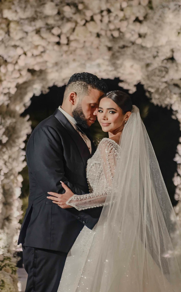 Pareja abrazada bajo un arco de flores blancas
