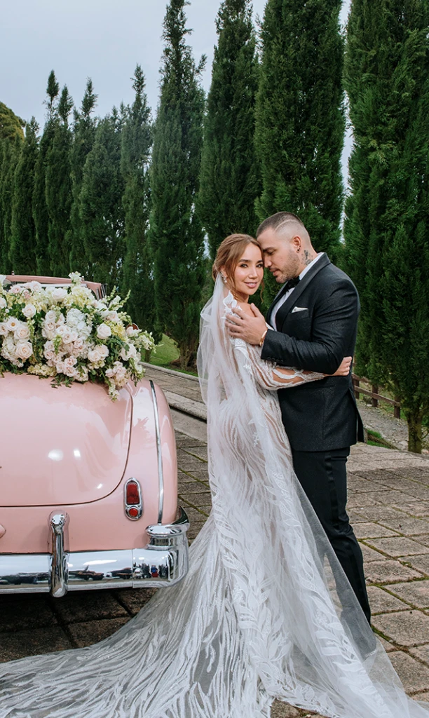 Recuerdo eterno de pareja casada frente a un auto rosa con arreglos florales