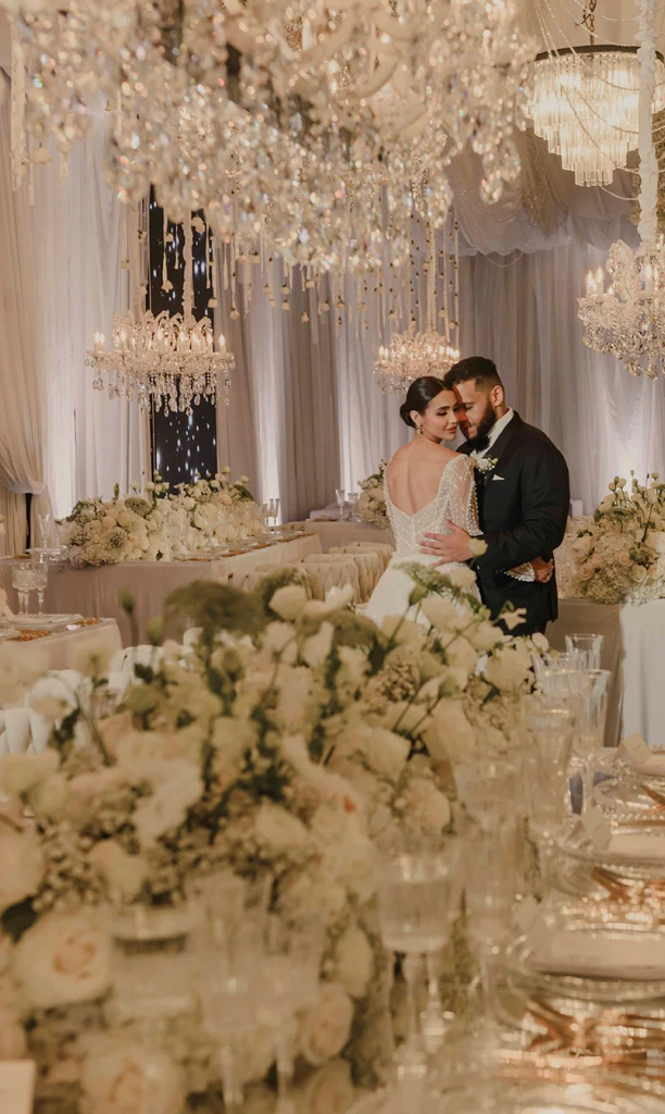 Pareja de esposos en un salón con candelabros blancos y mesas decoradas con flores
