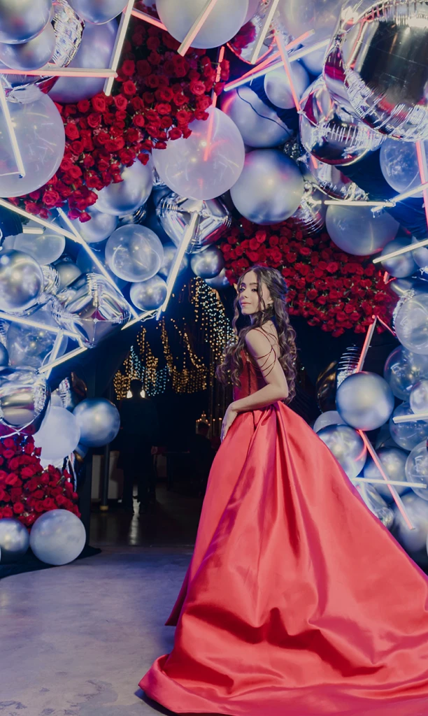 Chica bajo un arco de rosas rojas, globos plateados y luces led